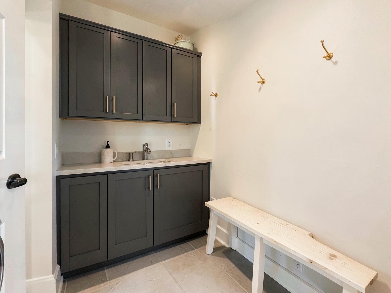 Charcoal laundry cabinets with oak bench and brass hooks